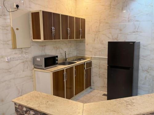 La cuisine est équipée d'un réfrigérateur noir et d'un évier. dans l'établissement شقق نورسين ان للشقق المخدومة, à Quai