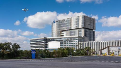 Un gran edificio de oficinas con un avión volando en el cielo. en Holiday Inn Express Kunming Changshui Airport by IHG, en Kunming