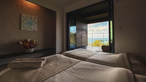 Dos camas en un dormitorio con una gran ventana. en Quan Sea Vista Retreat Japanese Room サウナ付き宿, en Onna