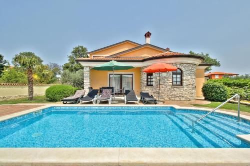 a pool with chairs and umbrellas in front of a house at Schöne Ferienvilla Morena Mit Pool in Kaštel