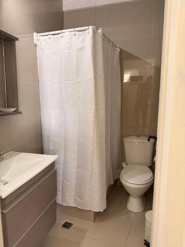 a bathroom with a toilet and a white shower curtain at Cocheras Ezeiza Victoria in Ezeiza