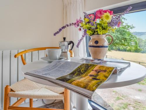 The Granary - Uk50401 في Llanstephan: طاولة مع صحيفة و مزهرية مع الزهور عليها