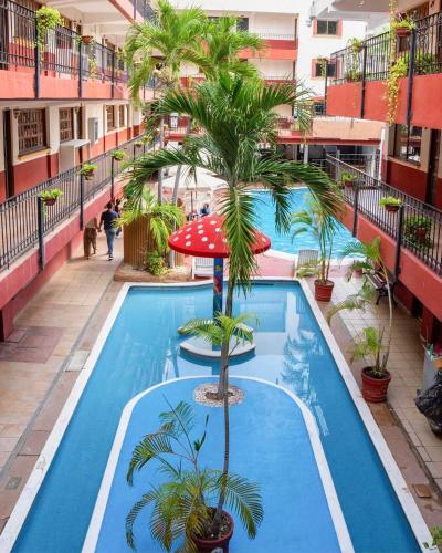 an apartment pool with a palm tree and an umbrella at Hotel Hacienda María Eugenia Acapulco in Acapulco
