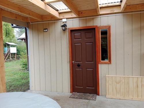 ein Haus mit einer braunen Tür und einem Fenster in der Unterkunft Pircas de Rucalhue Cabins for 4 people and Jacuzzi in Quilaco