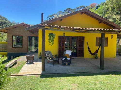 een geel huis met een hangmat ervoor bij Refúgio com Hidro, Lareira, Café da Manhã e Vista da Natureza in Santo Antônio do Pinhal