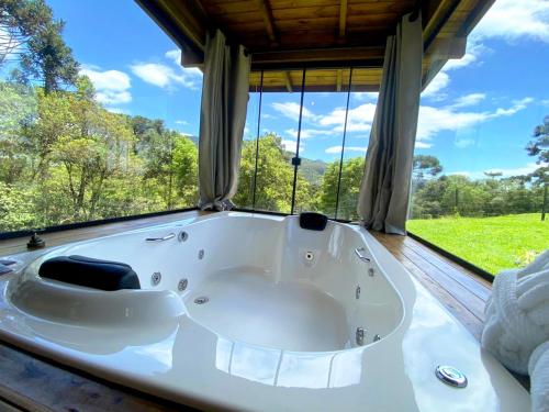 邦雷蒂鲁Chalé Eco das Aves próximo a vinícola Thera的大型窗户客房内的白色大浴缸