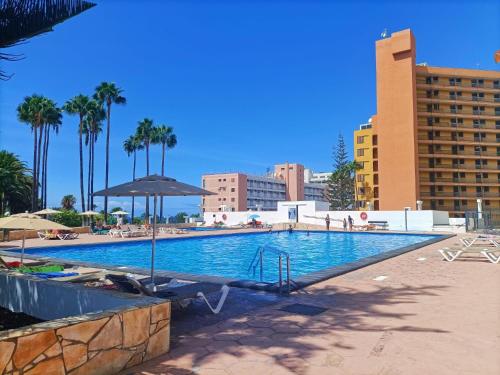 a swimming pool with an umbrella and palm trees and buildings at Casa Marazul in Costa de Adeje