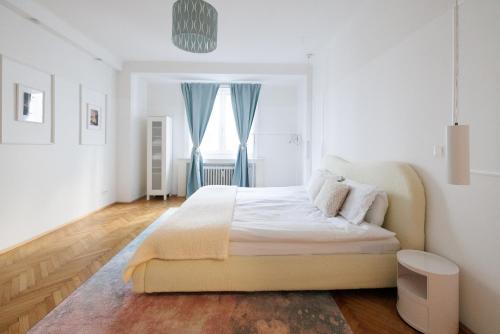 a white bedroom with a large bed with blue curtains at Operastreet Residences - Big Business Apartment in Vienna