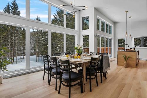 une salle à manger avec une table, des chaises et des fenêtres dans l'établissement Modern Waterfront Cottage on the Rouge River & Spa, à Rivière-Rouge