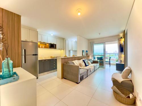 a kitchen and a living room with a couch at Apartamento em condomínio HOME CLUB, cozinha completa, PISCINA e JACUZZI aquecida, SAUNA, ACADEMIA, quadra de esportes playground infantil, salão de jogos a 40m da PRAIA e 15min do Beto Carreiro in Piçarras