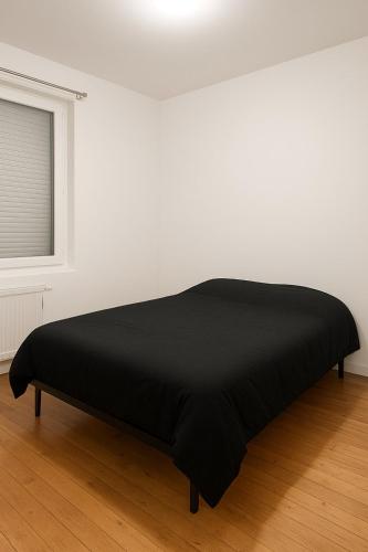a black bed in a white room with a window at Maison 2 chambres proche circuit 24h et toutes commodités in Arnage