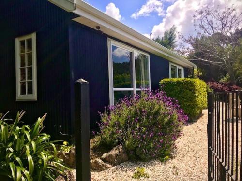 een blauw huis met een hek en bloemen ervoor bij Bay of Islands - Vineyard Cottage, chic private stunning view in Purerua