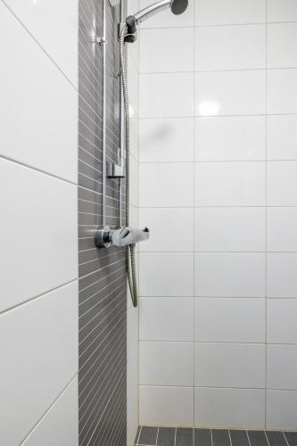 a shower in a bathroom with white tiles at Bright Loft Apartment Steps From Linnanmäki & Alppipuisto in Helsinki