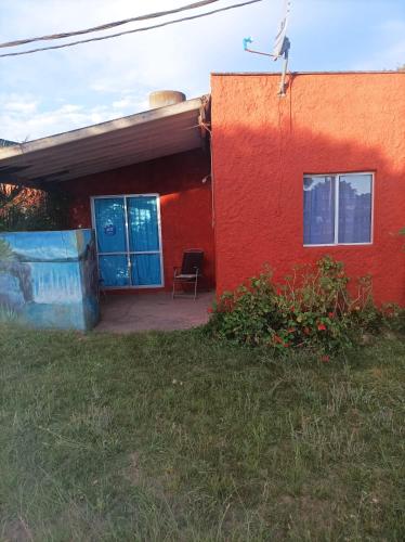 a red building with a blue door and a chair at Apartamento de sol a sol in Barra de Valizas