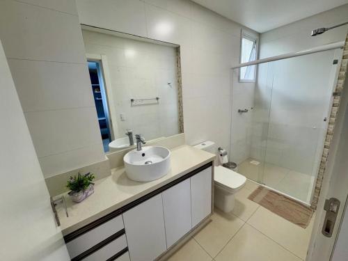 une salle de bain avec un lavabo, des toilettes et un miroir dans l'établissement Apto Frente Mar Itapema Canto da Praia, à Itapema