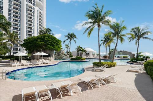 a swimming pool with lounge chairs and palm trees at Trump International Beach Resort - Sunny Isles Beach in Miami Beach
