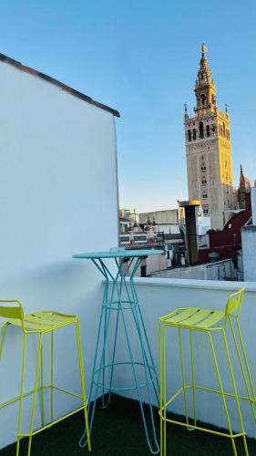 two chairs and a table on a balcony with a clock tower at Lukanda Hospec Olehousing in Seville