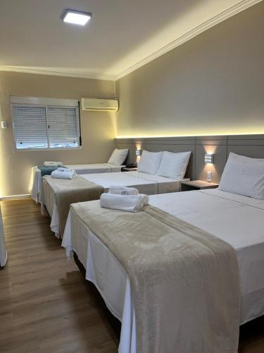 a hotel room with four beds with white sheets at Premier Palace Hotel in Araranguá
