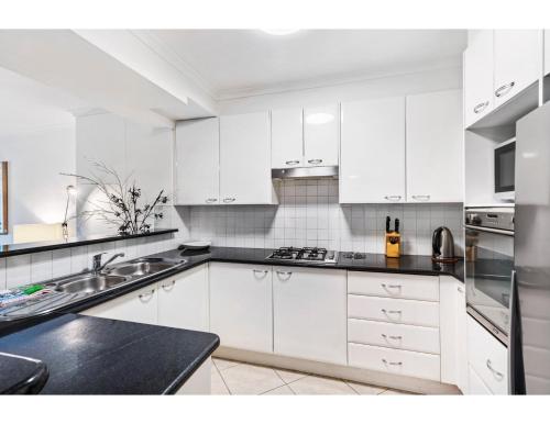 a white kitchen with white cabinets and black counter tops at Poolside 2-Bed Haven, Walk to City Centre in Sydney
