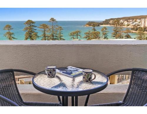 a table with two cups and a book on a balcony at Beachside Paradise - Ocean Views, Central Position in Sydney