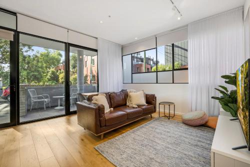 a living room with a leather couch and large windows at Bright Terrace Unit Next to Chapel St Dining in Melbourne