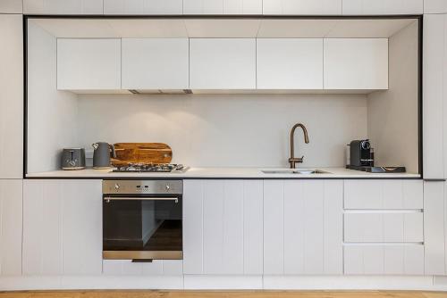 a kitchen with white cabinets and a sink and a stove at Bright Terrace Unit Next to Chapel St Dining in Melbourne