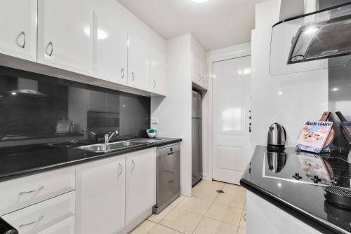 a kitchen with white cabinets and black counter tops at Spacious 3-Bed Apartment by the MCG in Melbourne