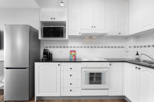 a white kitchen with white cabinets and a refrigerator at Modern Manly Apartment with Stunning Views, Pool in Sydney
