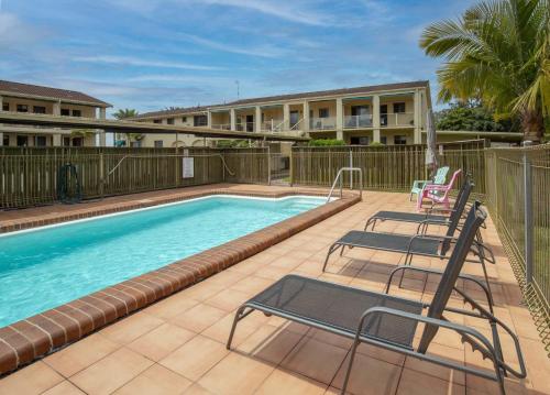 a swimming pool with two chairs next to a building at Seafront Getaway Studio, Great Location with Pool in Batehaven