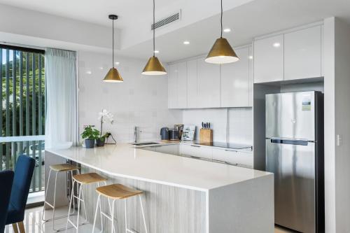 a white kitchen with a large white counter and stools at Spacious and Superb 3-bed Apartment in Brisbane