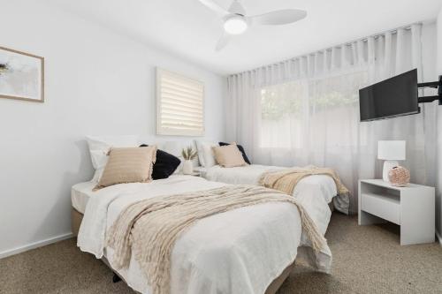 2 Betten in einem weißen Zimmer mit einem TV in der Unterkunft The Tides - Luxe Beach House Mornington in Mornington