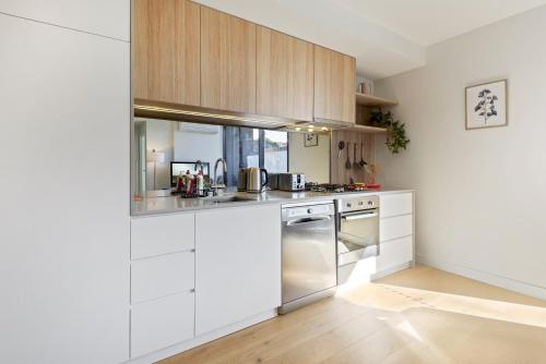 a kitchen with white cabinets and stainless steel appliances at Cosy 1-Bed with Private Balcony By Showgrounds in Melbourne