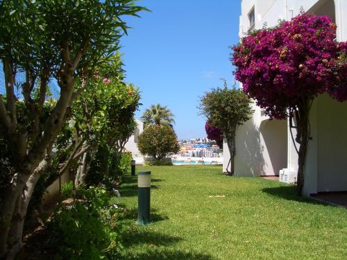 a green yard with pink flowers on the side of a building at Silmar in Albufeira