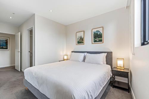 a white bedroom with a large bed and two lamps at Pristine 2-Bed Unit With Beautiful City Landscape in Melbourne