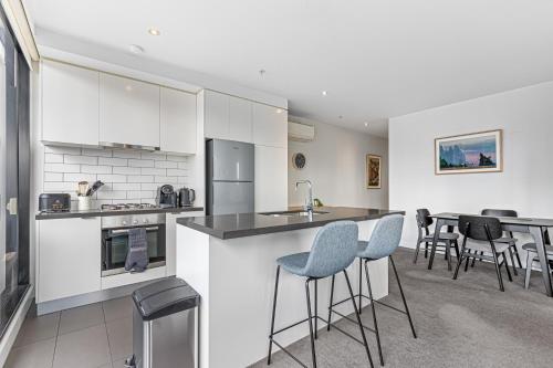 a kitchen with white cabinets and bar stools at Pristine 2-Bed Unit With Beautiful City Landscape in Melbourne