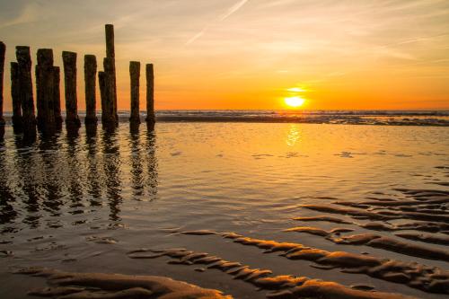 a sunset on the beach with poles in the water at Hotel Pannenkoekhuis Vierwegen in Domburg
