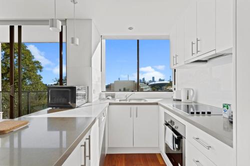 a white kitchen with white cabinets and a large window at Prime Location 2-Bed Apartment with Parking in Sydney