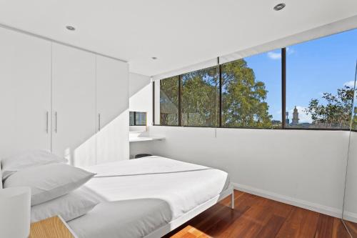 a white bedroom with a bed and a large window at Prime Location 2-Bed Apartment with Parking in Sydney