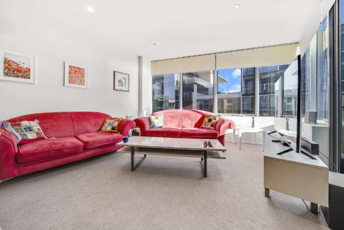 a living room with a red couch and a table at Canberra Lakefront 2-Bed with Pool, Gym & Parking in Kingston
