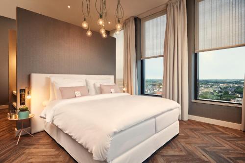 a bedroom with a large white bed and large windows at Van der Valk Hotel Nijmegen-Lent in Nijmegen
