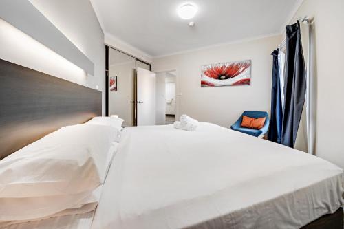 a bedroom with a large white bed and a blue chair at Comfy Lakeside 1-Bed with Secure Parking in Tuggeranong