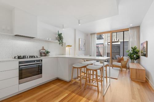 a kitchen with white cabinets and bar stools at Stylish 2-bed Victorian Terrace in Carlton in Melbourne