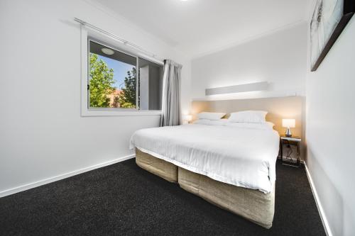 a white bedroom with a bed and a window at Spacious 2-Bed Conveniently by Lake Tuggeranong in Tuggeranong