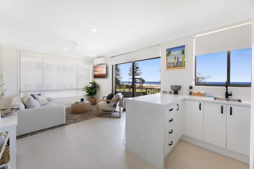a kitchen with white cabinets and a living room at Beachfront Studio with Balcony & Stunning Views in Gold Coast