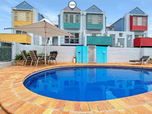 a pool with chairs and an umbrella and some houses at 3-Bed with Alfresco Dining & Pool in Batemans Bay in Batemans Bay