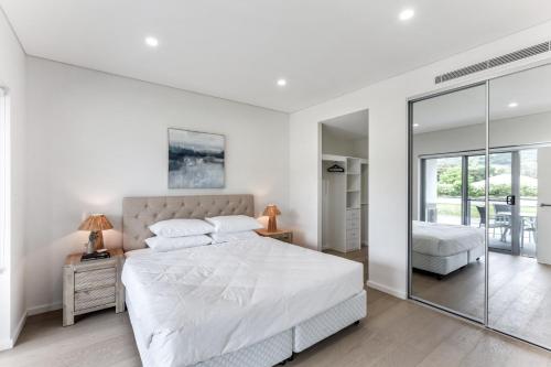 a white bedroom with a large bed and a mirror at First Floor 3-Bed Stunning Unit by The Ocean in Kiama