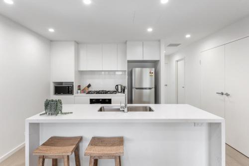 une cuisine blanche avec un évier et deux tabourets dans l'établissement Ground Floor Spacious Home in Kiama's Heart, à Kiama