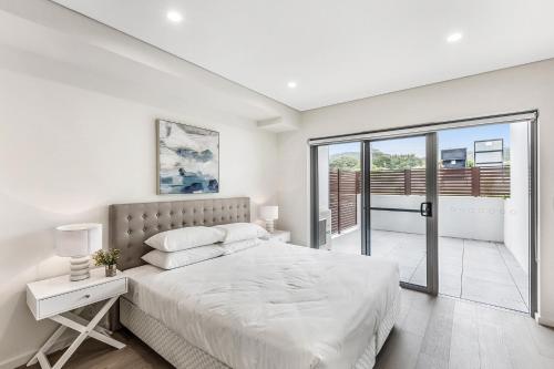 a white bedroom with a bed and a balcony at Ground Floor Spacious Home in Kiama's Heart in Kiama
