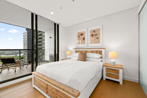 a white bedroom with a large bed and a balcony at Chic 1-Bed with Pool by River Ferry & Amenities in Sydney