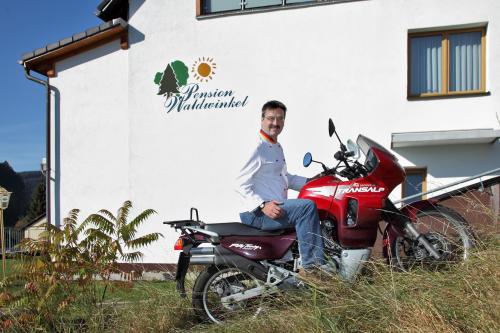 Ein Mann, der auf einem roten Motorrad vor einem Gebäude sitzt. in der Unterkunft Pension Waldwinkel in Lenzkirch